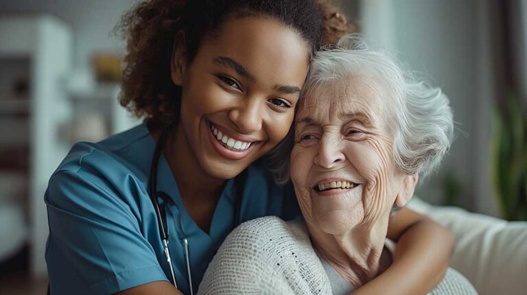 An older adult sits comfortably in a cozy living room, chatting with a caregiver over tea.